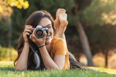 Gülümseyen genç kadın parkta fotoğraf çekmek için bir kamera ile.