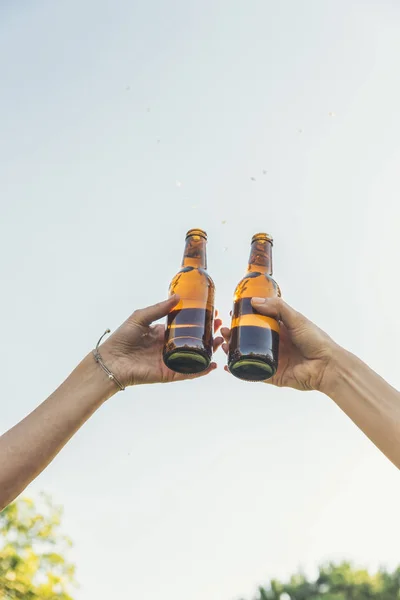 Female friends cheers clinking bottles of beer.