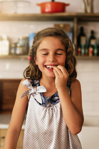 Little girl eating chocolate while preparing baking cookies.
