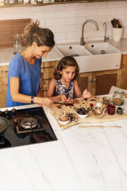 Küçük kız annesiyle mutfakta yemek pişiriyor..
