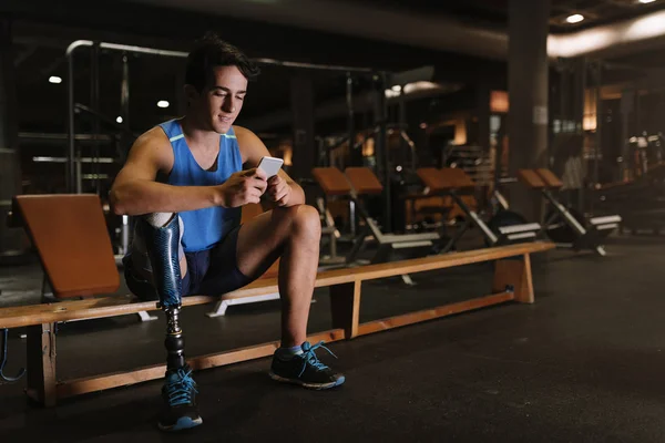 Joven discapacitado usando su móvil en el gimnasio . — Foto de Stock