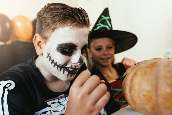 Niños felices disfrazados decorando una calabaza en casa . — Foto de Stock