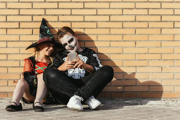 Des enfants heureux déguisés en utilisant le téléphone portable dans la rue . — Photo