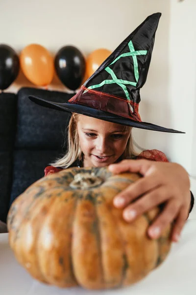 Hermosa chica disfrazada de bruja decorando una calabaza en casa . —  Fotos de Stock