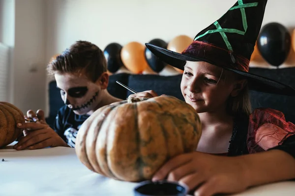 Niños felices disfrazados decorando una calabaza en casa . — Foto de Stock