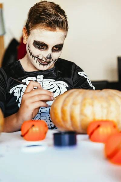 Niño feliz disfrazado decorando una calabaza en casa. Conc de Halloween —  Fotos de Stock