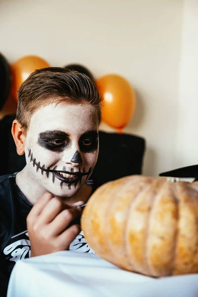 Niño feliz disfrazado decorando una calabaza en casa . —  Fotos de Stock