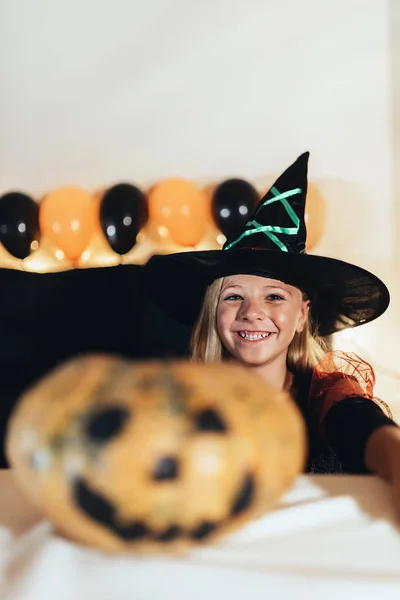 Hermosa chica disfrazada de bruja decorando una calabaza en casa . —  Fotos de Stock