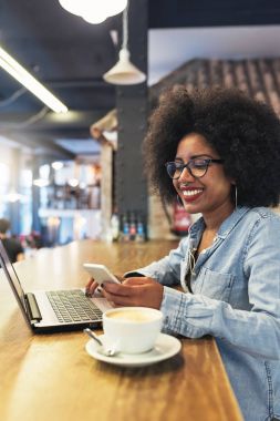 Cof içinde cep telefonu ve dizüstü bilgisayar kullanan güzel afro Amerikan kadın