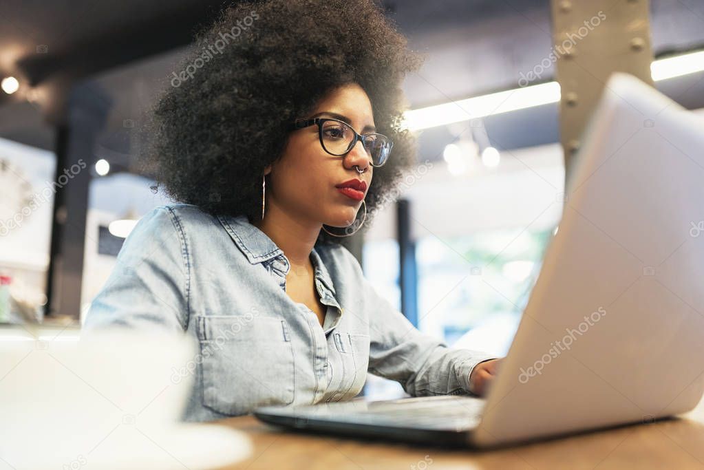 Beautiful afro american woman using mobile and laptop in the cof