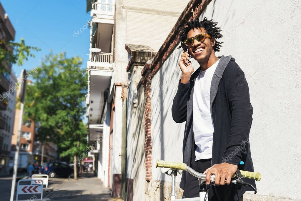 Afro young man using mobile phone and fixed gear bicycle.