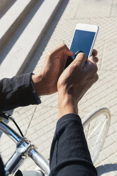 Primer plano del joven utilizando el teléfono móvil y la bicicleta de engranaje fijo . — Foto de Stock