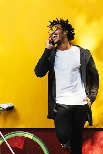 Afro young man using mobile phone and fixed gear bicycle.