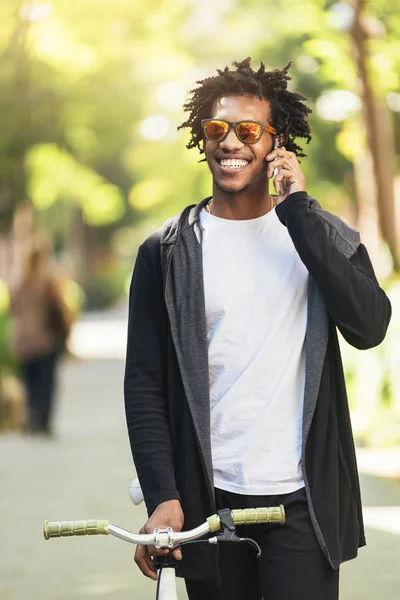 Afro giovane utilizzando il telefono cellulare e bicicletta a scatto fisso . — Foto Stock