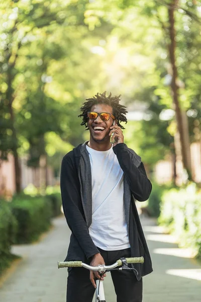 Afro jongeman met behulp van de mobiele telefoon en fixed gear fiets. — Stockfoto