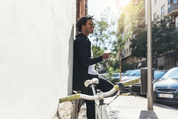 Pemuda Afro menggunakan ponsel dan sepeda roda tetap . — Stok Foto