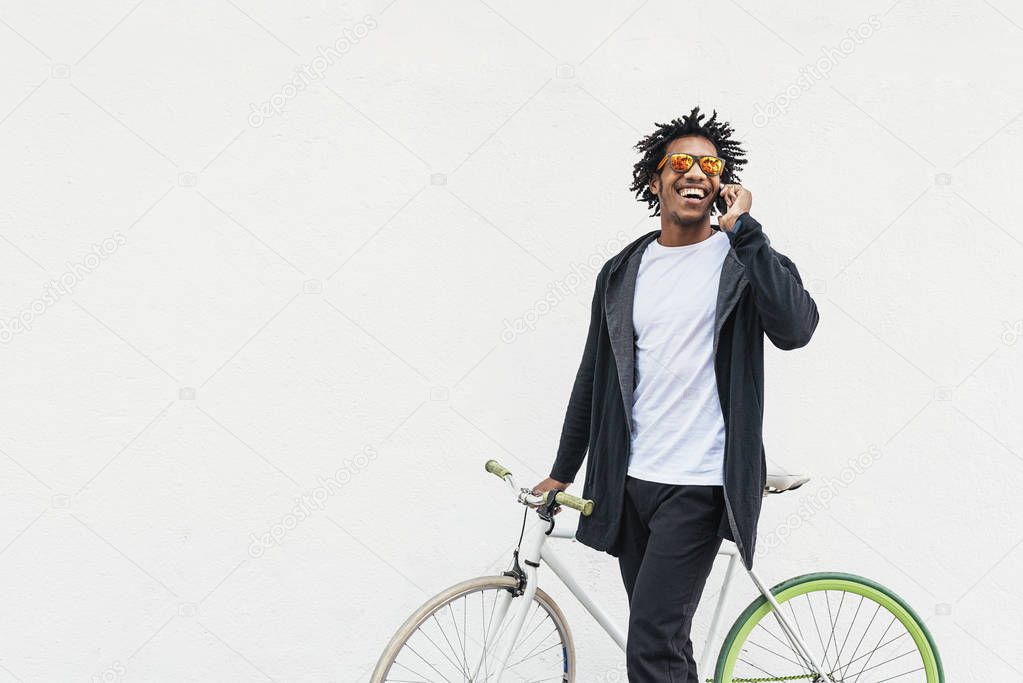 Afro young man using mobile phone and fixed gear bicycle.