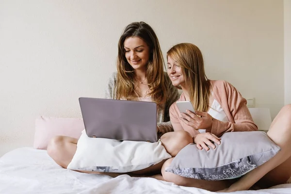 Gorgeous friends using the laptop and mobile in the bedroom.