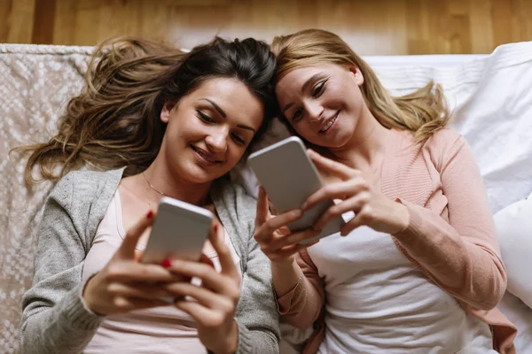Wunderschöne Freunde mit dem Handy im Schlafzimmer. — Stockfoto