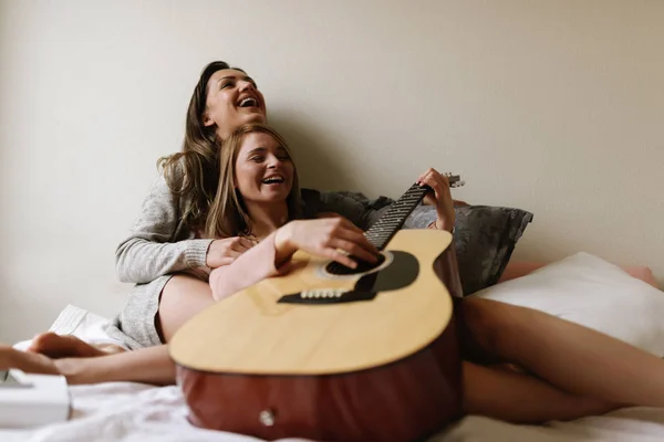 Gorgeous friends playing the guitar in the bedroom.