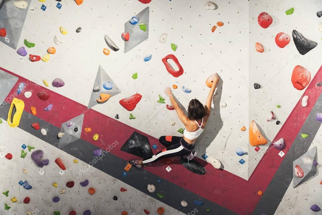 Woman practicing rock climbing on artificial wall indoors.