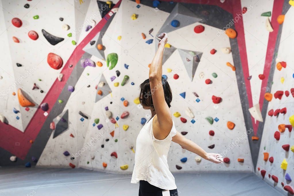 Woman training for practice rock climbing on artificial wall indoors.