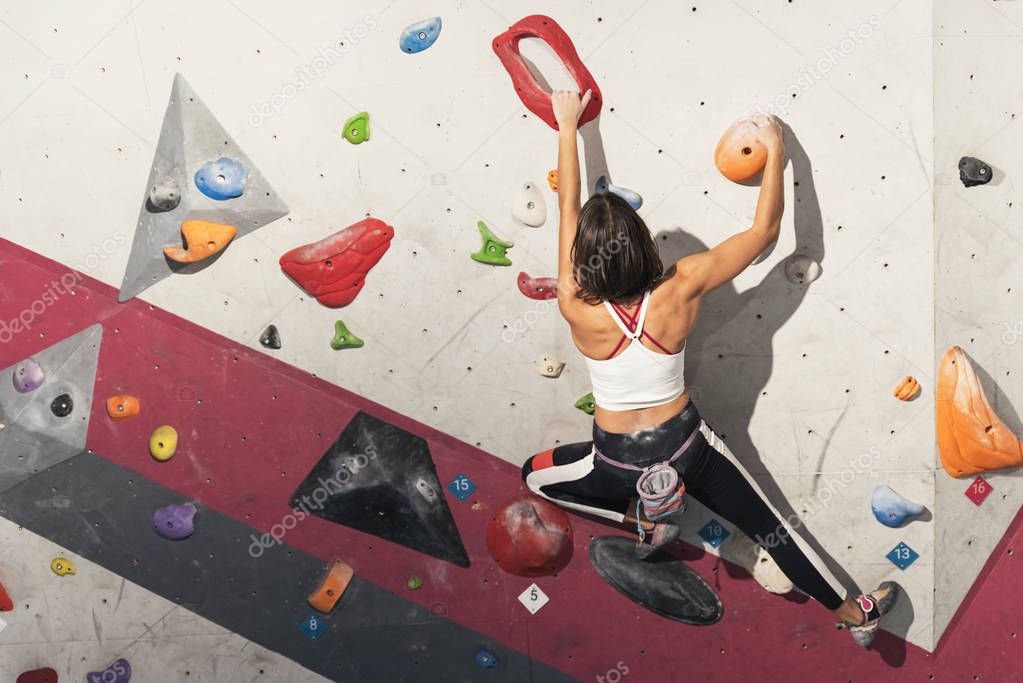 Woman practicing rock climbing on artificial wall indoors. Active lifestyle and bouldering concept.