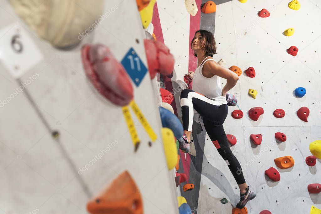 Woman practicing rock climbing on artificial wall indoors. Active lifestyle and bouldering concept.