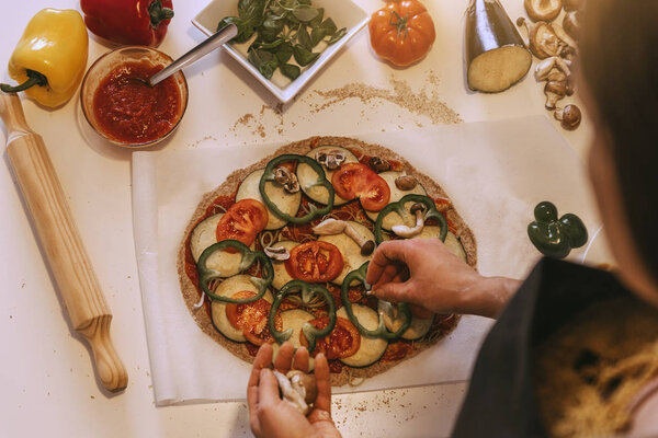Woman adding healthy ingredients to pizza.