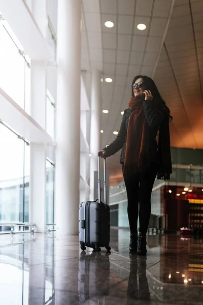 Femme marchant avec une valise à l'aéroport tout en utilisant le mobile . — Photo