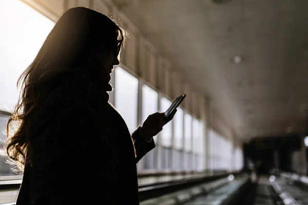 Kobieta nie do poznania, korzystania z telefonu komórkowego w terminalu lotniska. — Zdjęcie stockowe