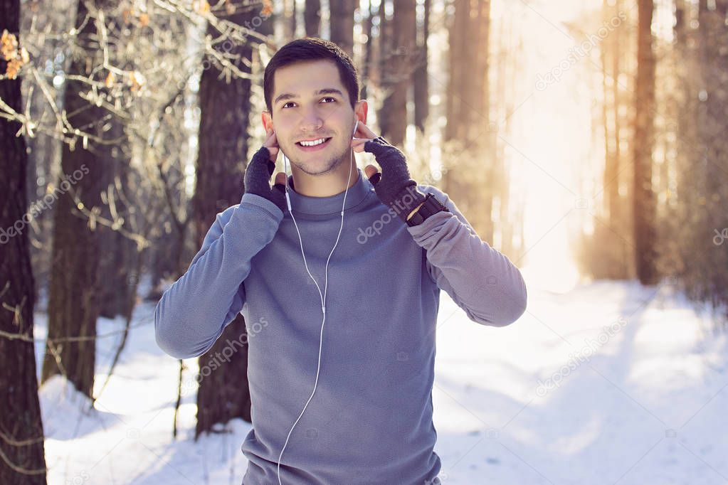 Sports man listening music in forest and smiling. Winter.