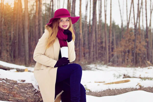 Молодая, красивая и стильная рыжеволосая девушка в пальто и шляпе держит термостат. Мода . — стоковое фото