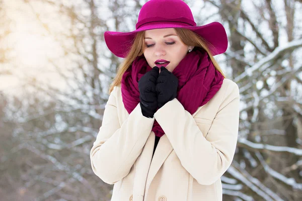 Молодая, красивая и стильная рыжеволосая девушка в пальто и шляпе греет руки в лесу. Мода . — стоковое фото