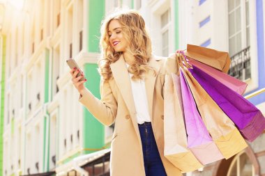 Şık, güzel sarı saçlı gülümseyen kız telefonunu kullanarak shoppings. Mutlu alışveriş.