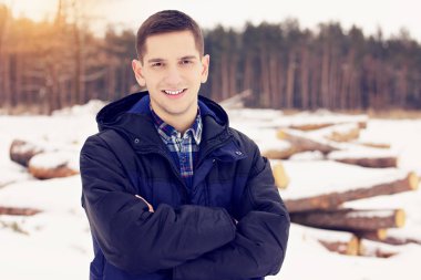 Yakışıklı, şık ve gülümseyen genç adam ceket ayakta ormanın içinde. Erken Bahar güneşli bir gün. Erkek moda.