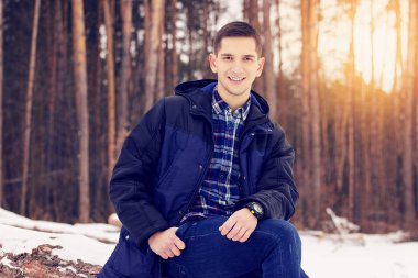 Yakışıklı, şık ve gülümseyen genç adam orman ormanda oturan ceketli. Erken Bahar güneşli bir gün. Erkek moda.