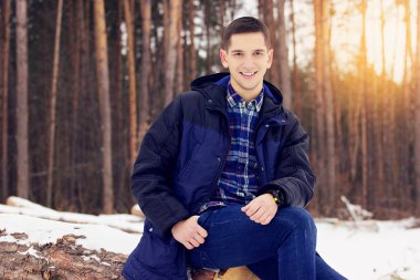 Yakışıklı, şık ve gülümseyen genç adam orman ormanda oturan ceketli. Erken Bahar güneşli bir gün. Erkek moda.