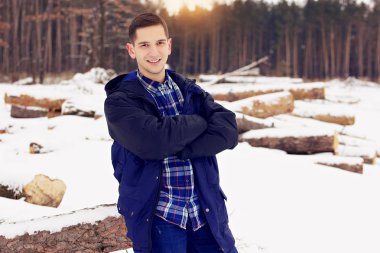 Yakışıklı, şık ve gülümseyen genç adam orman ormanda oturan ceketli. Erken Bahar güneşli bir gün. Erkek moda.