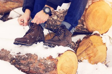 Yakışıklı, şık ve genç bir adam bağları ayakkabı bağı ve ormandaki ağaçların üzerinde oturan. Erken Bahar güneşli bir gün. Erkek moda.