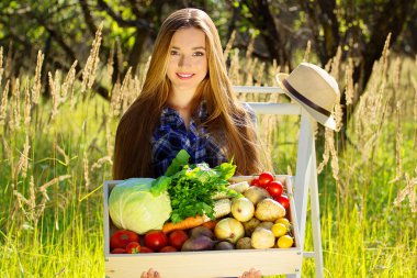 Güzel ve genç gülümseyen kız ahşap kutu sebze dolu tutmak. Yaz hasat.