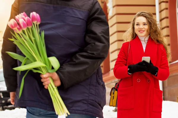 Romantik Tarih. Erkek arkadaşı için arkasından çiçekler gizler. Güzel genç çift birlikte şehir sokaklarında yürüyüş. Bahar.