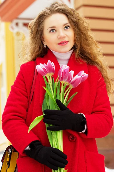 Bella ragazza bionda giovane ed elegante in cappotto rosso contenente fiori. Primavera . — Foto Stock