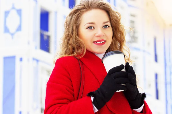 Молодая, красивая и стильная блондинка в красном пальто, пьющая кофе на городской улице. Женская мода . — стоковое фото