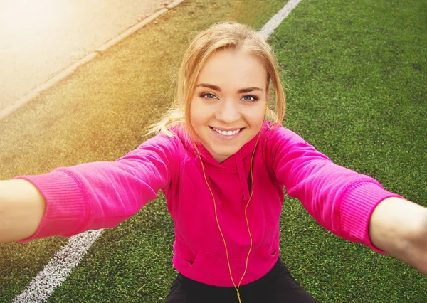 Junge schöne blonde Haare Fitness-Mädchen beim Selfie mit einer Kamera auf dem Stadion. Sommersport. — Stockfoto