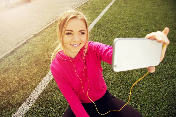 Fiatal gyönyörű szőke haja fitness lány csinál vele telefonon, a stadion selfie. Nyári sport tevékenység. — Stock Fotó