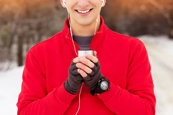 Gülümseyen yakışıklı sporcu çay içme ve parkta müzik kırmızı kazaklı. Açık hava etkinliği.