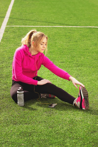 Fiatal gyönyörű szőke haja fitness lány csinál, stretching a stadion. Nyári sport tevékenység. Zöld stadion fű háttér. — Stock Fotó