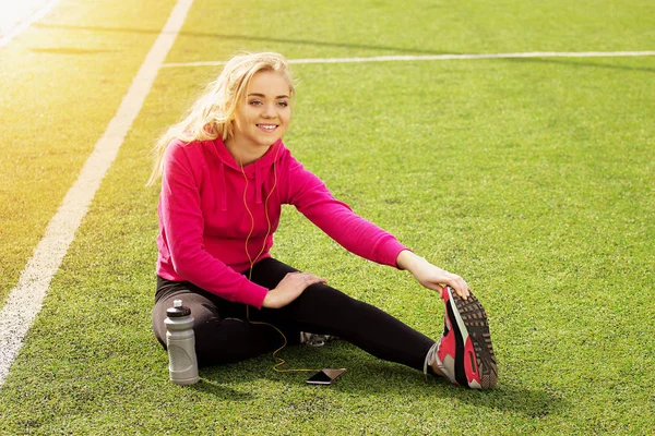 Fiatal gyönyörű szőke haja fitness lány csinál, stretching a stadion. Nyári sport tevékenység. Zöld stadion fű háttér. — Stock Fotó