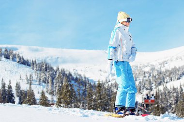 Beyaz ceketli genç güzel kız mavi Kayak pantolon ve googles snowboard karlı dağlarda sürme başında. Kış sporları.